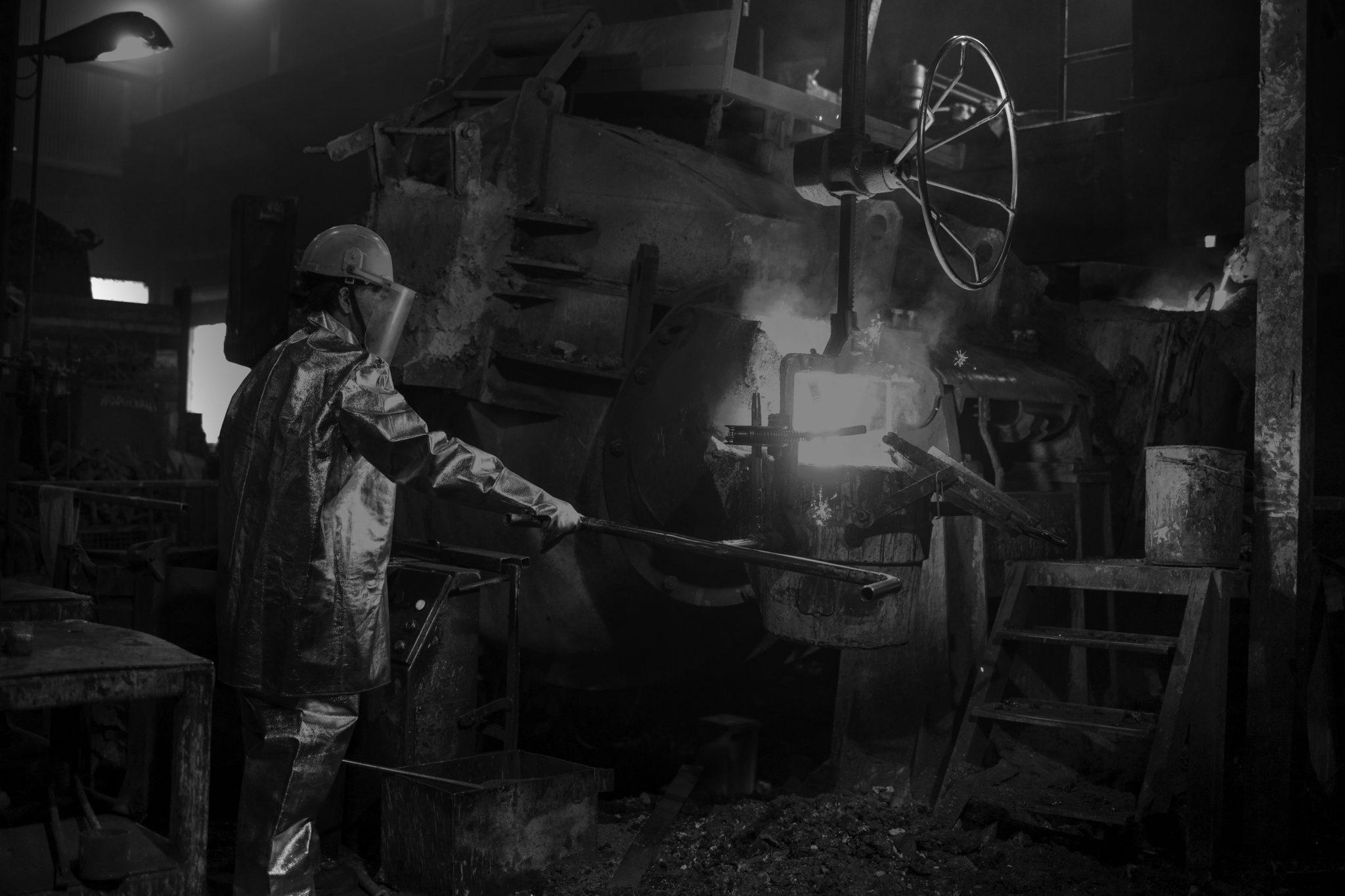 Hardworking in foundry. Workman in temperature protection suit pouring liquid metal into the bucket. Steel production.